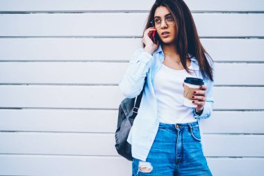 Elinde telefon konuşma açık havada beyaz promosyon arka plan üzerinde reklam için ayakta sırasında. toplantı düzenlemek için çekici öğrenci optik gözlükler ve kahve. Cep üzerinde konuşmak erkek