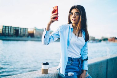 Şık gözlük telefon sosyal ağlar modern şehir köprüsü üzerinde hafta sonu gezisi sırasında ayakta paylaşmak için fotoğraf yapma içinde hipster blogger. Kısa mesaj reklam için yer alan kopyalama