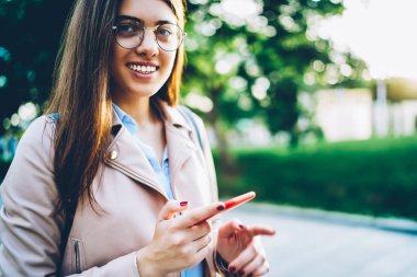 Gözlük kamera açık havada kopyalama alanı alanı metnin yakınında sokakta yürüme mesafesinde gülümseyen süre modern smartphone aygıtında yeni uygulama yükleme çekici neşeli öğrencinin kırpılmış portre