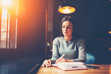 Yetenekli öğrenci ödev yapmak ve deneme alanı filtre efekti ile coworking içinde masada oturan sınav hazırlama için Not Defteri'nde aşağı yazma. Kopyalama alanı alanı reklam metin iletinizi için