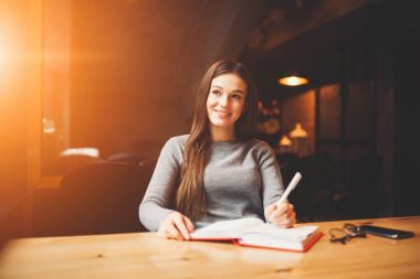 Uzağa bakarak ve aşağı kendi günlük kapalı alan coworking defada şiirler yazarken gülümseyen pozitif esmer öğrenci. Ev ödevi düşünceli kadın düşünme. Metin reklam tanıtım alanı