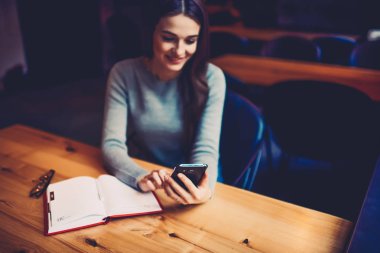 Beyaz sayfalar ile not etmek ve modern smartphone aygıt online sohbet ile wome'nın el üzerinde seçin. Esmer hippi kız gönderme sms mesajı hücresel coworking içinde oturan arkadaşına gülümseyen