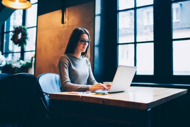 Yüksek hızlı internet bağlantısı ve kafede oturan modern dizüstü bilgisayar kullanarak ders üzerinde gözlük yetenekli öğrenci. Grafik tasarımcı netbook klavye gözlük yoğunlaştı