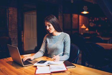 Dizüstü bilgisayar aygıt Webinar izliyor ve Not Defteri'nde bazı bilgiler online kurslar kafede oturan sırasında dikkat çeken esmer öğrenci. Bilgisayar eğitim ve sınav için hazırlanıyor hippi kız 