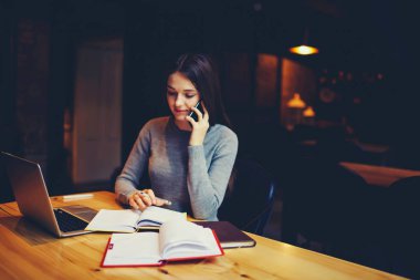Cep telefonu üzerinde arkadaşıyla konuşurken ve muhasebe yapma genç işkadını raporları dizüstü bilgisayar aygıt ile ahşap masa kendi kahve dükkanında otururken bağlı 4 g kablosuz internet