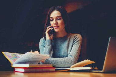 Çekici genç kadın modern smartphone üzerinde iletişim kurma ve Üniversitesi'nde yaklaşan sınavlar için hazırlanıyor. Edebiyat kitapları ile oturma ve hücresel üzerinde konuşurken eğitim esmer hippi kız