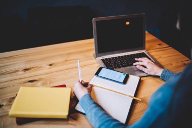 Telefon ve kitaplar ile ahşap masa başında oturan öğrencinin arkadan görünüm kırpılmış. Kadın el sahte reklam alanı ile kablosuz internet'e bağlı modern dizüstü bilgisayarın klavye yazarak