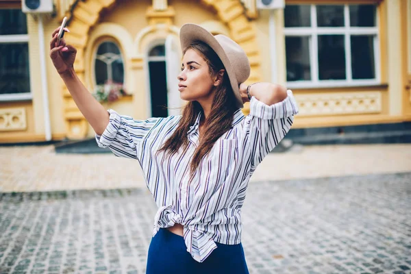 有魅力的时髦女孩坐在时髦的帽子的著名设计师站在街头假扮自拍智能手机相机 博客作者通过电话在社交网络中共享照片 — 图库照片