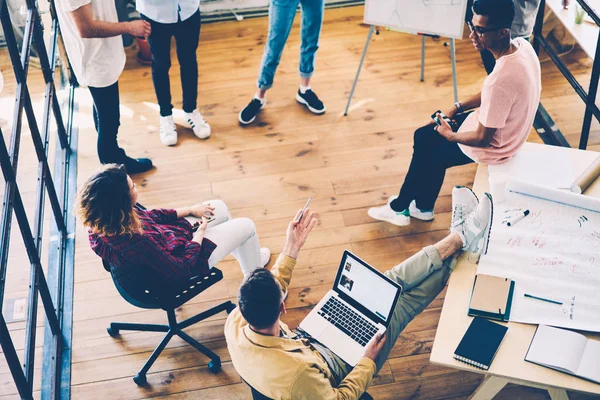 Experienced marketing expert dressed in trendy clothing explaining to colleagues general working concepts while browsing interesting information in websites on laptop computer with mock up screen