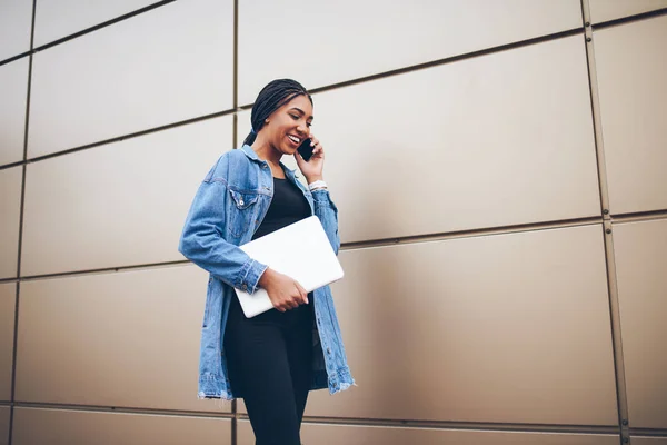 时髦的美国黑人时髦的女孩在牛仔夹克谈论智能手机漫步在户外沿宣传区的文本 国际学生用手提电脑在电话里交流 — 图库照片