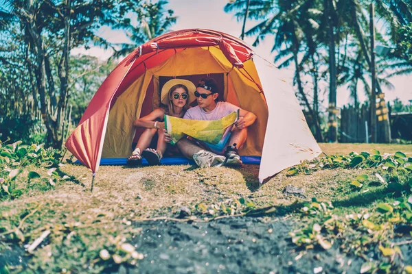 Young romantic couple camping on tropical island recreating in tent during journey trip in summer weekends ,active hipster guys discussing route for hiking reading map spending vacations together