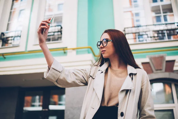 物思いにふける魅力的な内気な少女 春の日にスクロール 都市設定の背景に画像を作る流行の服装で女性観光客のソーシャル ネットワークに写真を共有しているスマート フォン カメラで Selfie を作る — ストック写真
