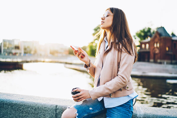 Молодая женщина с брюнетками, наслаждаясь отдыхом, сидя на открытом воздухе в городской обстановке и загружая пост в интернет-блоге на современной телефоне.Женщина делает оплату онлайн на cellular.Copy пространстве области
