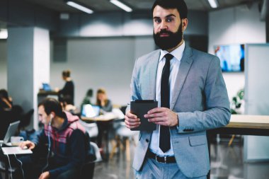 Modern dokunmatik yüzey kamera ile profesyonel geliştiriciler inşa Office dururken bakarak elinde tutan formal giyim emin sakallı icra müdürü portresi giymiş