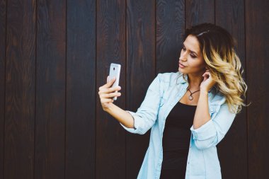 Genç iyi blogger reklam promosyon arka plan yanında dururken modern telefon kamera selfie alarak arıyorum. Sevimli öğrenci bahar yürüyüşte, kentsel ayarı sırasında fotoğraf yapma