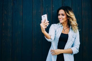 Selfie akıllı telefon kamera ve paylaşım yapma genç gülümseyen hippi kız görüntü sosyal ağ takipçileri ile yapılmış. Resim ayakta duvara promosyon arka plan ile yakın alarak şirin mutlu kadın