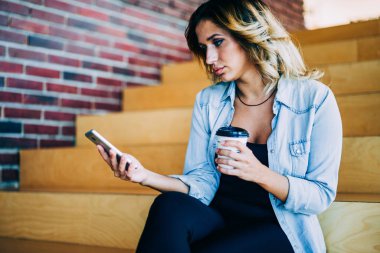 Güzel kadın şık giyim telefon kablosuz internet'e bağlı ilginç video izlerken giymiş. Web sitesinde cellphone Haberler okuma ve kahve tutan dalgın hippi kız