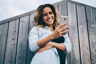 Web sitesinde cep telefonu komik video izlerken çekici neşeli öğrenci bağlı 4 g için Internet sırasında ayakta dışında. Hippi kız ücretsiz vakit Street iyi bir ruh hali ve gadget ile gülümseyen