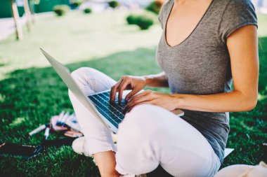 Kadın dizüstü arama bilgilerini online dersler sırasında açık havada park, tarama web sitesi Üniversitesi Kampüs çim üzerinde zaman harcamak öğrenme için netbook kullanan kadın yazarak görüntü kırpılmış