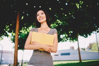 Pozitif genç kız öğrencinin üniversite kampüsü literatürde güneşli günde eğitim, hippi kız zevk hobi bitirme okuma roman sonra açık havada park hayal gülümseyen favori kitap