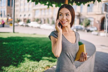 Esmer kadın cep telefonunuzda ile servis operatörünüze Şehir Parkı, kitap ile pozitif genç kadın arkadaş arıyorum uzak kopya alanı yürüme ile telefon konuşmayı ayakta konuşurken gülümseyen