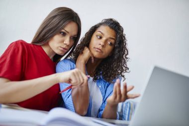 Zeki çok ırklı kız öğrenci bilgi dizüstü bilgisayar, ağdaki genç kadınlar izlerken okuma kurs proje için fikirler tartışırken öğretici yazıhane içinde konuşmayı birlikte