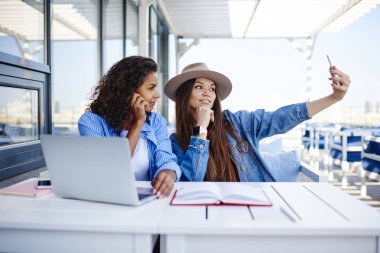 Selfie akıllı telefon kamera ve Bloglama ödev, hippi kız telefonu birlikte boş vaktinizi alarak resim için poz gülümseyen kafe teras oturma yapma genç en iyi arkadaşlar