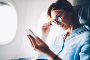 Çekici kadın telefon uçak kabin internete bağlanmak için ağ haber tarama mobil, genç kadın Gezgin ağlarda haber okuma üzerinde uçuş sırasında vakit uçakla seyahat