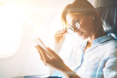 Çekici kadın telefon uçak kabin internete bağlanmak için ağ haber tarama mobil, genç kadın Gezgin ağlarda haber okuma üzerinde uçuş sırasında vakit uçakla seyahat