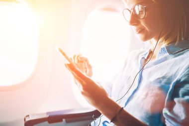 Genç kadın meloman mobil müzik ve Aksesuar, kadın kulaklık smartphone üzerinden müzik keyfi uçağın tahta üzerinde eğlenceli kullanarak birinci sınıf kabinde uçuş sırasında en sevdiğiniz şarkıları dinleme