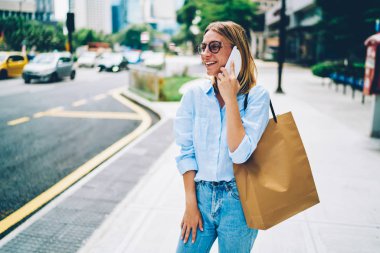 Kentsel ortamda cep telefonu konuşurken tanıtım mockup bulunduðu alışveriş çantası taşıyan gezici, genç gülümseyen kadın telefon konuşmayı şehir merkezinde yürüyüş zevk neşeli hippi kız