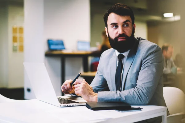 有信心的胡子执行主任穿着优雅的灰色西装 看着坐在数字计算机在工作场所和工作的新项目在办公室内部 商业广告宣传区 — 图库照片
