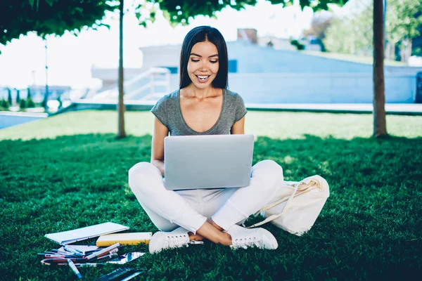 Smiling female student searching information for coursework project on laptop learning outdoors in college campus, positive young woman designer working on freelance satisfied with free schedule