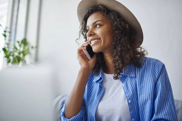 Smiling young african american woman in trendy hat satisfied with service contact mobile operator,cheerful dark skinned hipster girl having telephone conversation with friend during free time