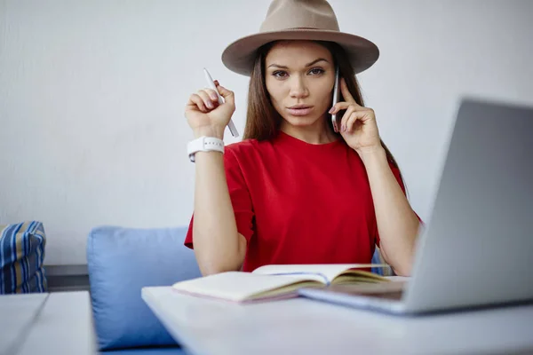 Portrait of serious young woman analyzing information during mobile consultancy with operator sitting near laptop computer,confident female having telephone conversation making banking operations