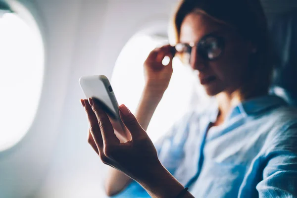 有吸引力的妇女乘飞机旅行在飞行期间从网络上阅读新闻从移动 年轻女性旅行者浏览网络新闻在电话为连接互联网在航空器客舱 — 图库照片