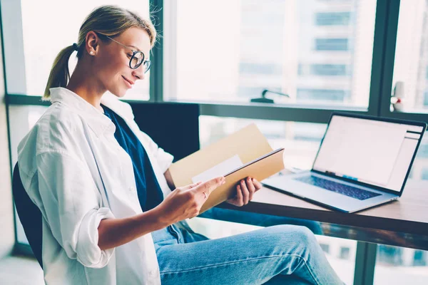 眼鏡満足絶頂金融で陽気な若い女性レポート フォルダーのオフィスビルで働く広告のための空白の画面領域をデジタル コンピュータ ガジェットでデスクトップに座っての読書 — ストック写真