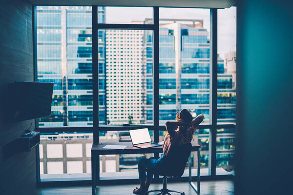 Задний вид женщины фрилансер отдыхает после завершения работы в офисе на ноутбуке с пустым экраном. Студент, наслаждающийся отдыхом, смотрит фильм на компьютере дома с вечерним видом на город
