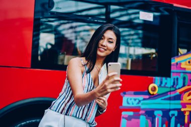 Çekici kadın turistik gezi buss arka planda, şehir turu mobil seyahat blog takipçileri ile paylaşmak için fotoğraf yapma zevk mutlu Asyalı kadın ayakta smartphone selfie yapma