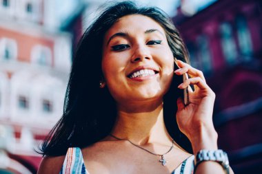 Telefon görüşmesi yapmak için uluslararası gezici bağlantısı kullanarak kamera kadın bakarak gülen, neşeli esmer Asyalı kız açık havada telefon görüşmesinde bulgu dışarı iyi haberlerle heyecanlı