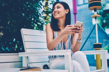 Asyalı kız Smartphone kullanarak bilgi kafe teras üzerinde boş zaman etkinlikleri sırasında oturan gözatmak gülümseyen, neşeli kadın trendy giyim ağlarda arkadaşlarınızla sohbet iletileri gönderme ve manifatura