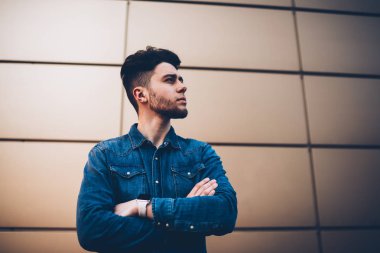 Kendine güvenen hipster adam uzakta duvar promosyon arka plan üzerinde ciddi yakışıklı genç adam kopyalama alanı alanı üzerinde çapraz kol ile reklam veya içerik için ayakta poz şık kot gömlek arıyor