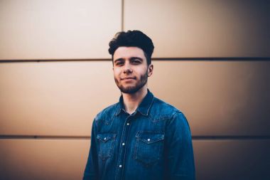 Reklam, yakışıklı delikanlı için rahat kıyafet ve kameraya bakarak trendy saç modeli ile duvar kopyalama alanı alanı üzerinde poz şık denim gömlek giymiş emin hipster adam portresi