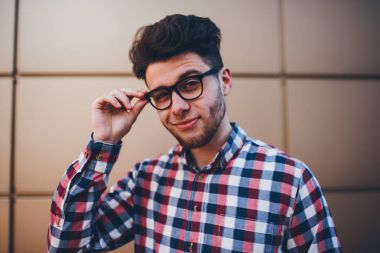 Son moda gözlük ve ekose gömlek duvar arka plan, yakışıklı genç hipster adam açık havada şık gözlükler kameradan bakarak ayakta açık havada poz genç teen öğrenci portresi