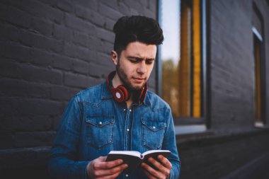 Dalgın genç yakışıklı kot gömlek düşünmeye arsa okuma ilginç kitap açık havada, zeki düşünceli erkek öğrenci bilgi öğrenme düşkün edebiyattan analiz üzerinde konsantre