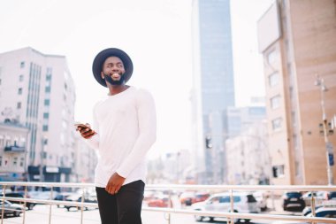 Açık havada ellerini, cep telefonu ile yürürken güzel havanın tadını neşeli Afrikalı-Amerikalı adam turist karanlık gülümseyen erkek seyahat gezi sırasında cep telefonu online navigasyon kullanarak derili