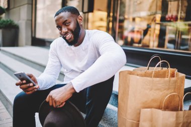 Afrika kökenli Amerikalı adam bekle geri bildirimi web depolama hizmeti esmer adam ödeme online yolu ile hareket eden memnun online alışveriş yapmadan gülümseyen, satın alma için merdiven bekleyin oturan portresi