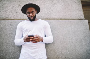Uzun kollu gömlek cep, ağ üzerinden haber markası okuma için kopya alanı ile dalgın afro Amerikan adam koyu tenli blogger telefon açık havada dinlenme uygulama yükleme konsantre