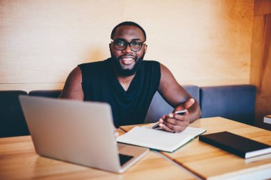 Uzak iş smartphone üzerinde mesaj gönderme, esmer erkek Yöneticisi'nde telefon yazılım güncelleme kamera bakarak gözlük gülümseyen kafe iç neşeli afro Amerikalı işadamı portresi