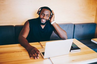 Gülümseyen koyu tenli hipster adam laptop, netbook üzerinde zamana Cafe online video izlerken neşeli afro Amerikalı adam şarkı indirme serbest zaman sırasında müzik dinlerken kulaklık